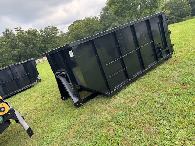 Large black dumpster on grassy field under cloudy sky