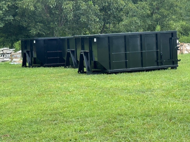 Two large green dumpsters sit on a lush grassy area