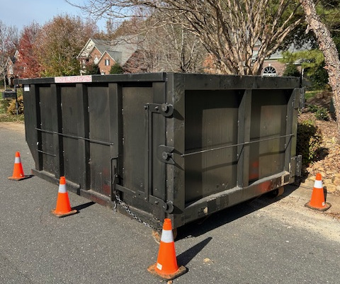 A large black dumpster sits on a residential street